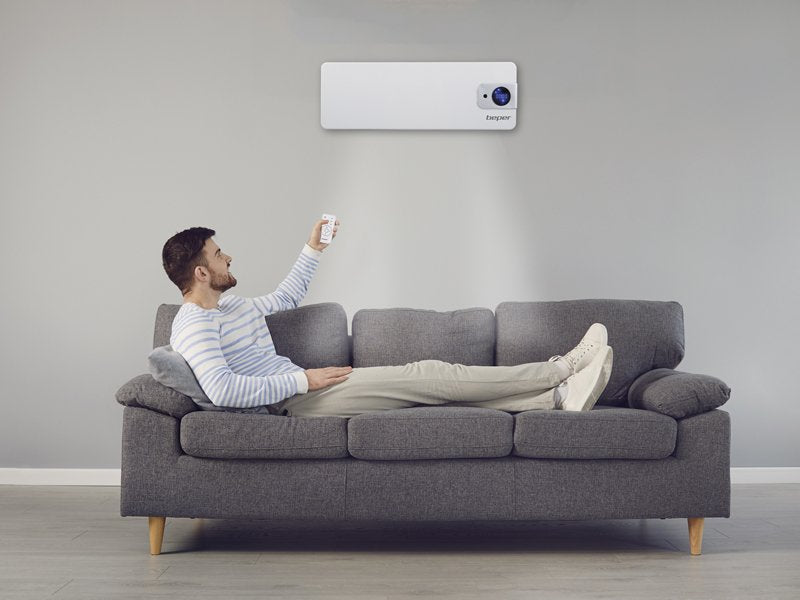 Mann på sofa bruker fjernkontroll til veggmontert varmevifte i moderne stue