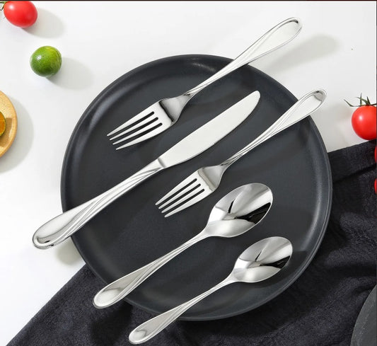 Elegant bestikk i rustfritt stål på svart tallerken, omgitt av tomater og lime